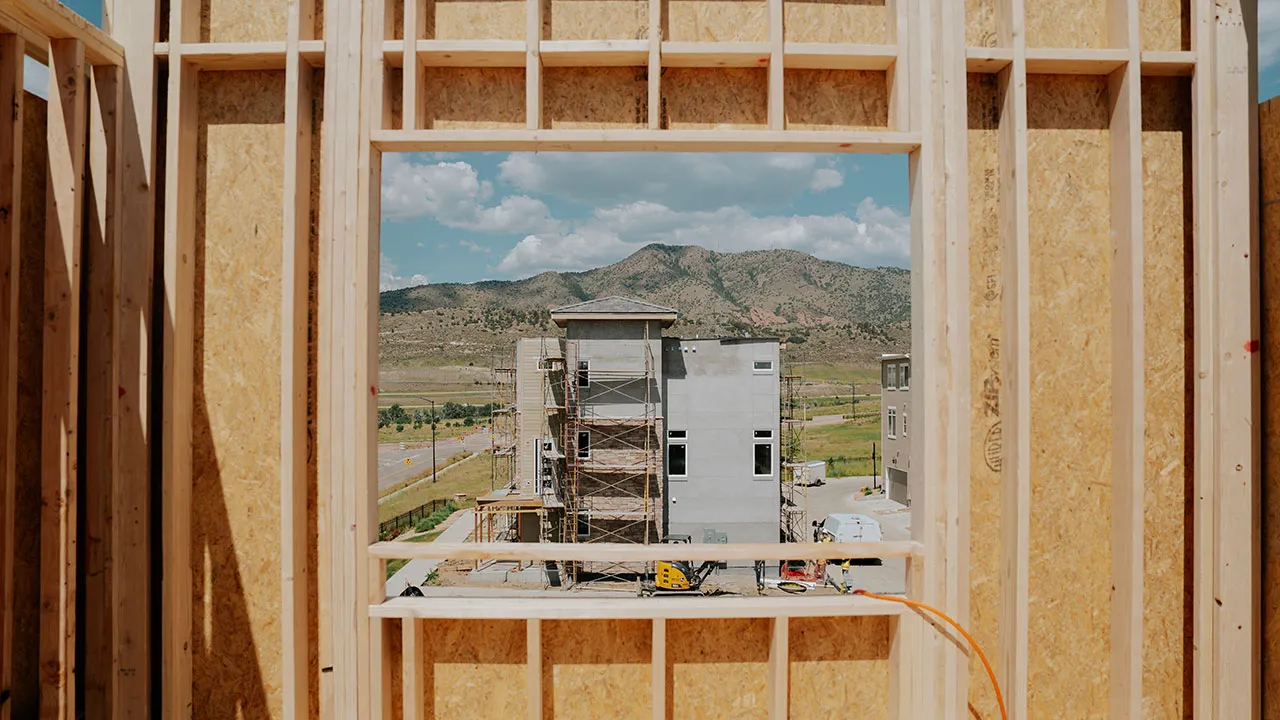 View through a framed wall opening toward a home under construction
