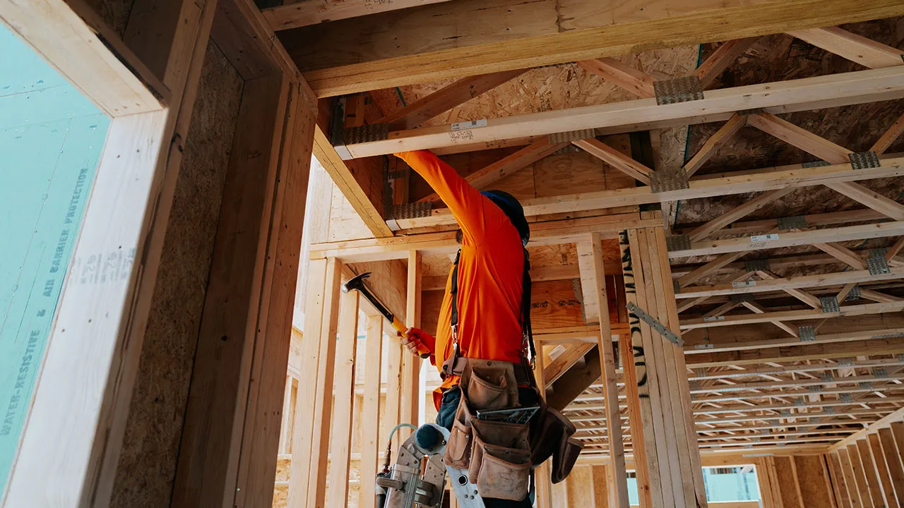 Crew member installing interior framing beneath roof trusses