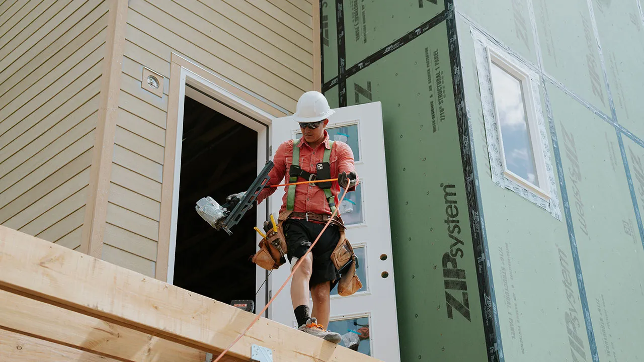 Crew member carrying tools while stepping out onto exterior framing